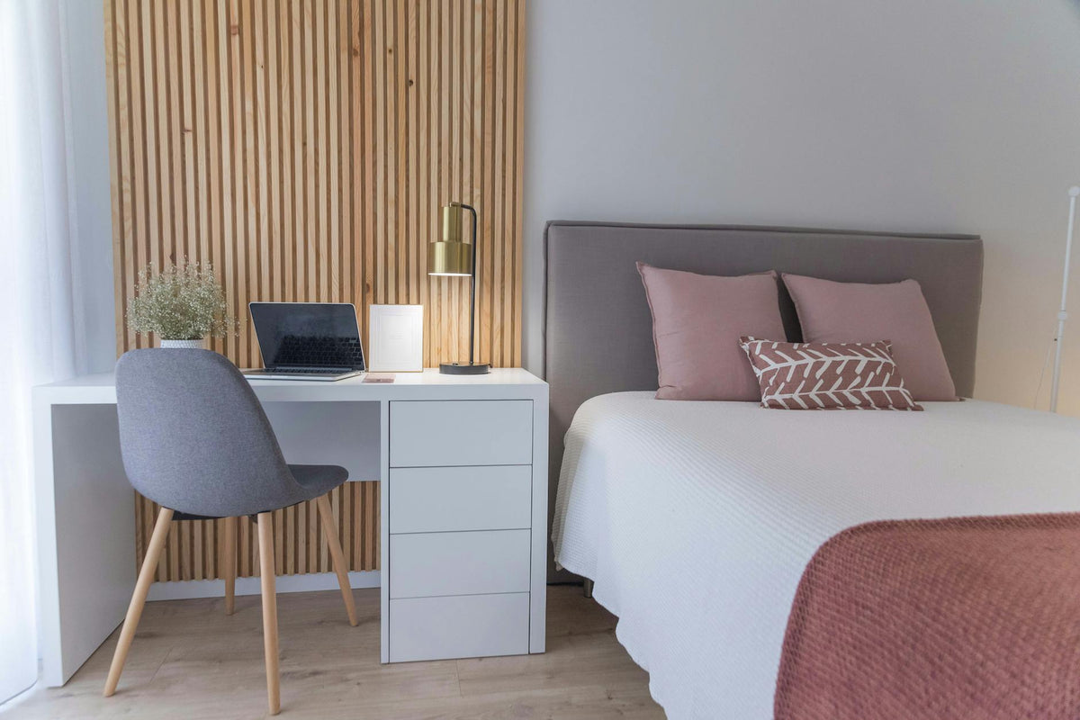 Modern minimalist bedroom in Lisbon with workspace, featuring a laptop and soft pastel decor.