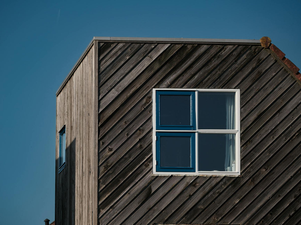 Minimalist wooden house exterior with blue window against clear sky.