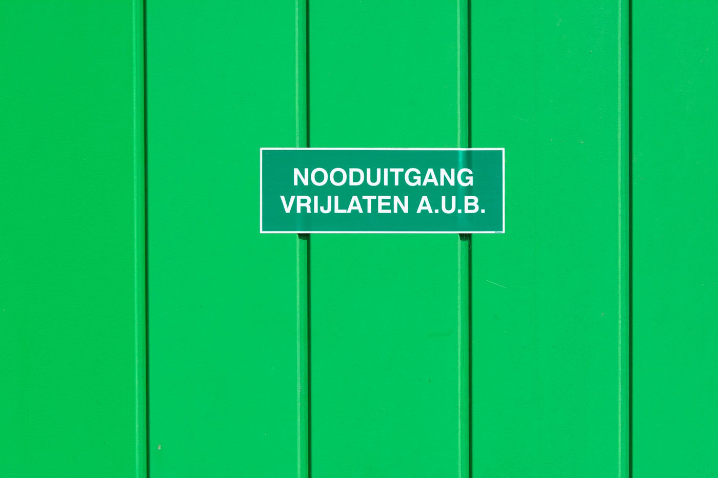 A green metal wall featuring an emergency exit sign in Dutch. Perfect for safety-themed graphics.