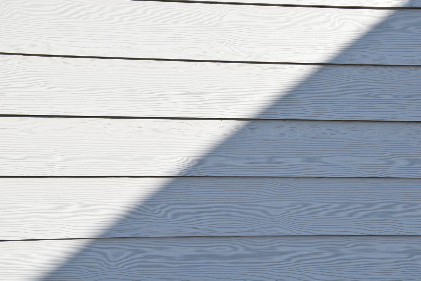 Close-up of a white wooden wall featuring a bold diagonal shadow.