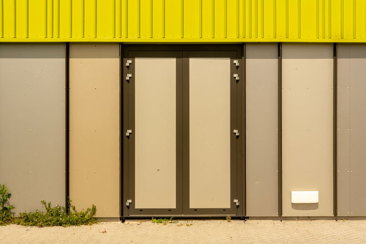 A vibrant yellow and gray industrial building facade with a minimalist design double door.